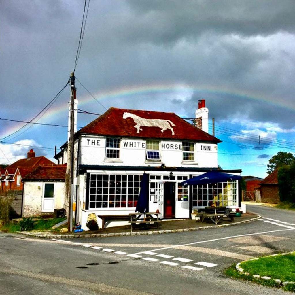 The White Horse Inn under a rainbow, with the white horse painted on its roof
